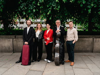 Fem musikere står foran trær